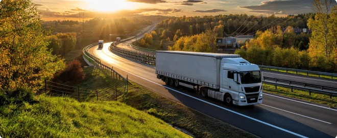 White trucks driving on the highway winding through forested landscape in autumn colors at sunset