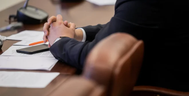 One of politician sitting by table with his hands over document during political summit or conference