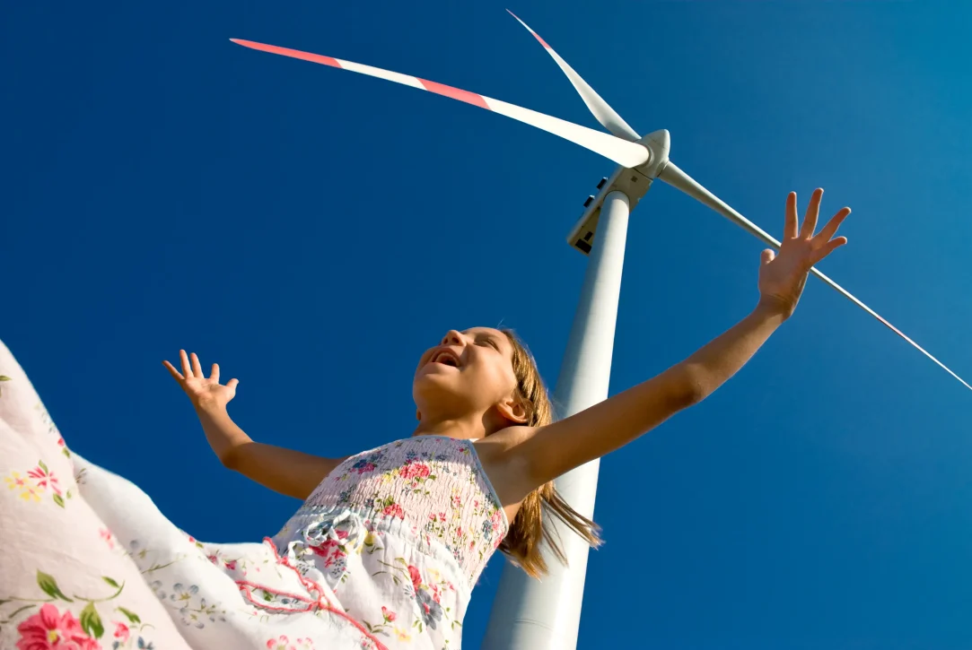 Smiling girl with arms outstretched below a windmill