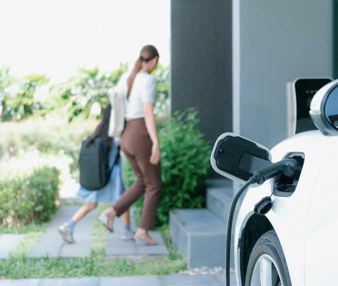 Focus EV car charging at home charging point with blurred background of family