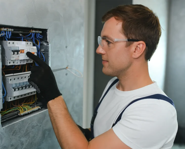 A male electrician works in a switchboard with an electrical connecting cable